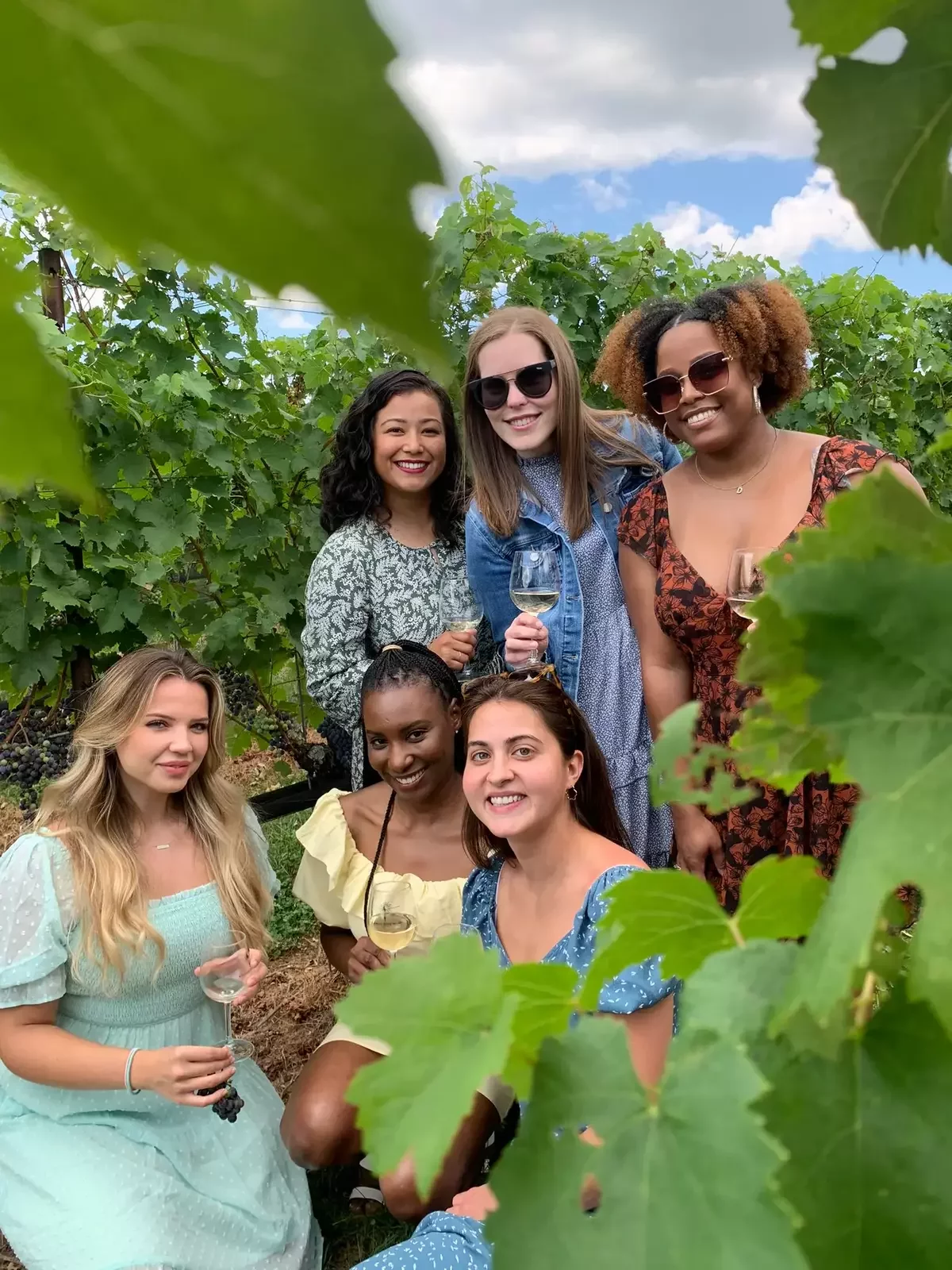 Corporate group enjoying a private wine tasting in a Virginia vineyard, posing with wine glasses among the vines.