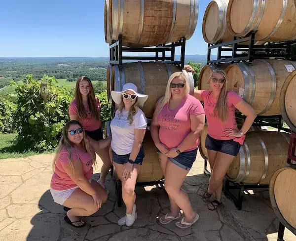 Group of friends celebrating a private wine tour at Bluemont Winery, surrounded by barrel stacks and scenic views of Virginia wine country.